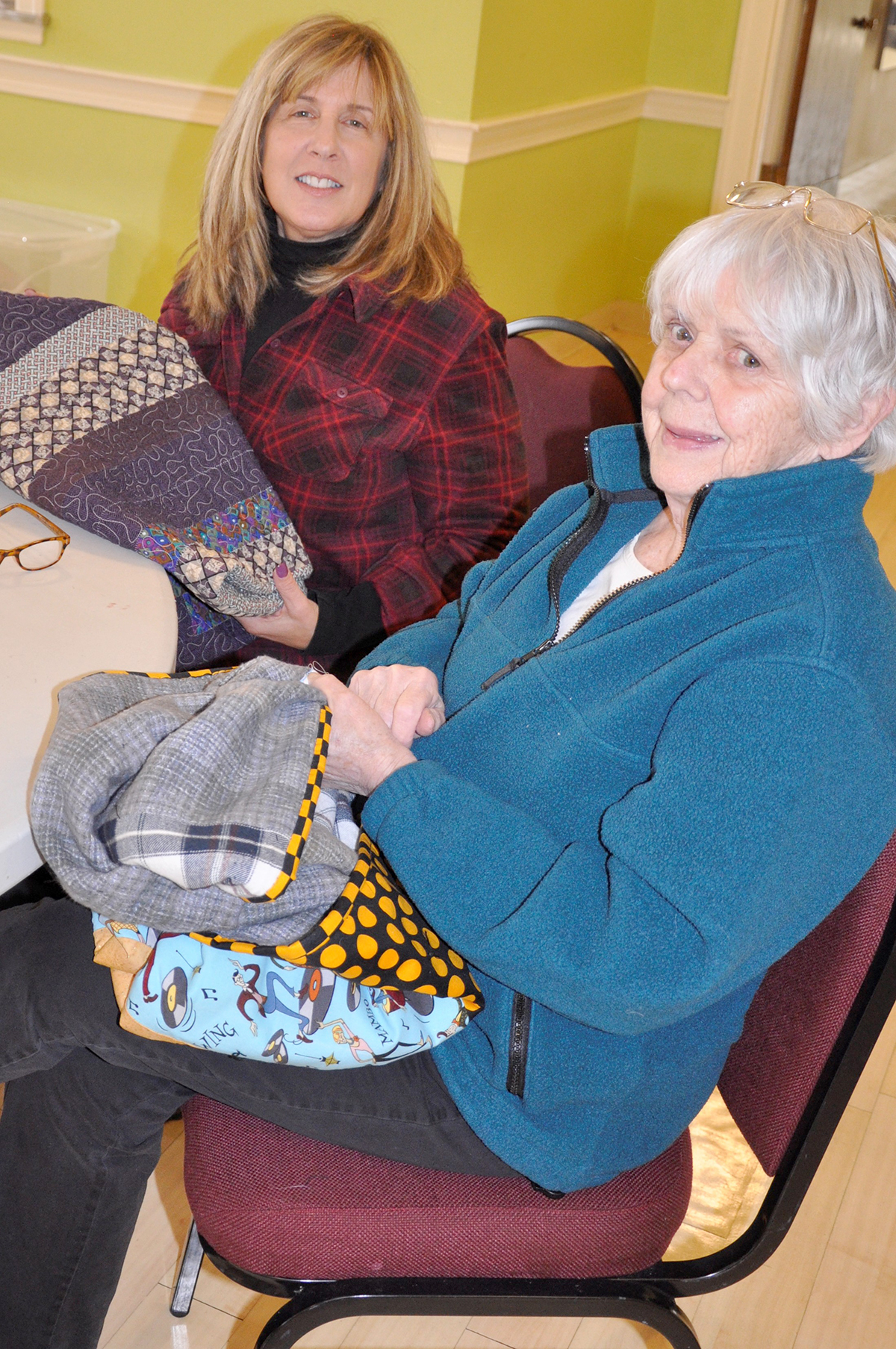 At the MLK Day charity quilt-a-thon, Helen Sicotte (at right) and newcomer Cindy Levine happily hand-sewed project labels to completed comfort quilts that will be distributed later to a Boston-based infusion unit. (Photo/Deborah Burke Henderson)