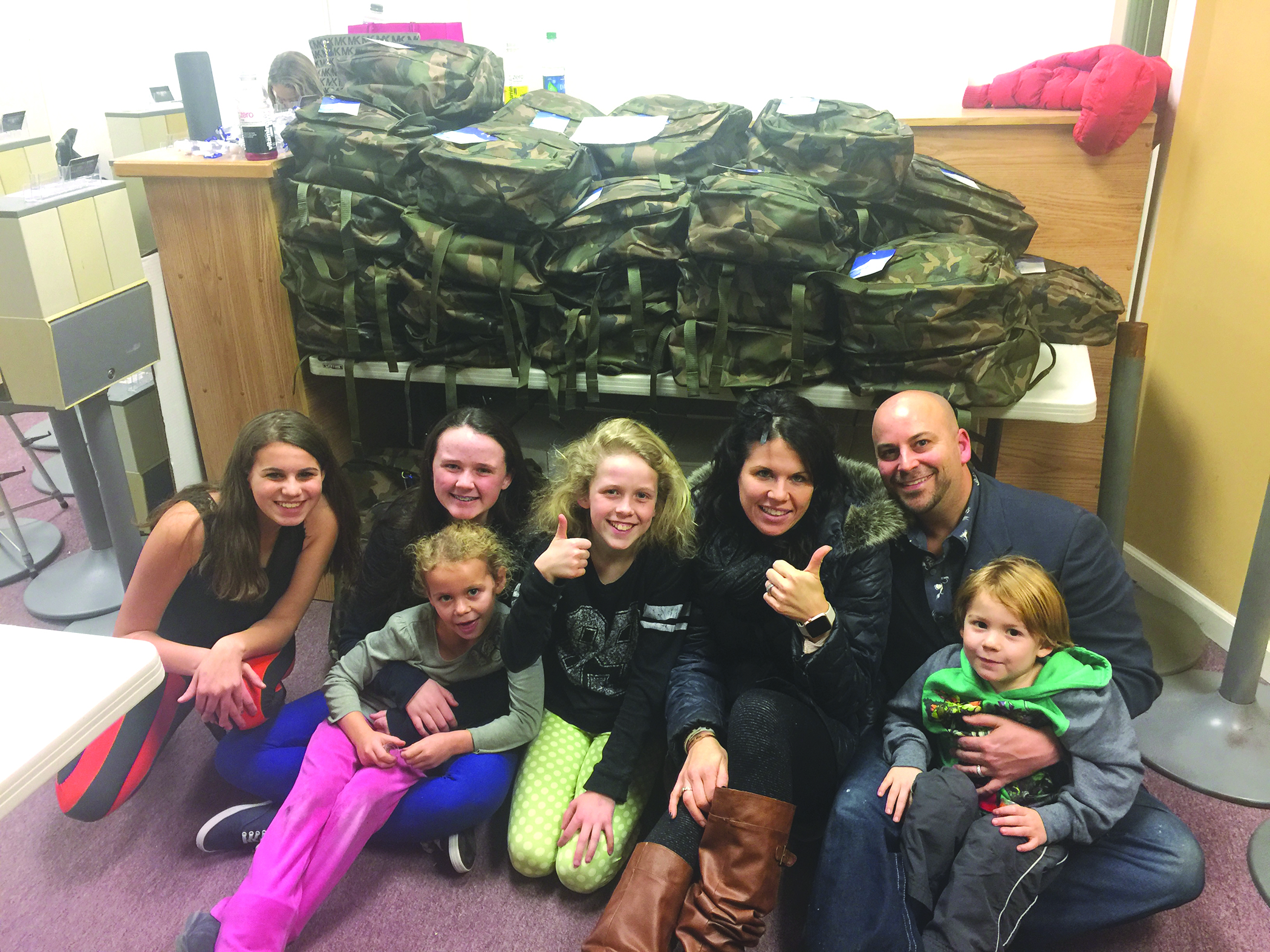 On December 10th, these volunteers helped pack backpacks full of personal hygiene items, blankets, water bottles and comfort items for Make Change for Change’s “Backpack Brigade” to hand out to people living on Boston’s streets on Christmas Eve. From left to right, Sophia Williams, 13, Caileigh Judson, 15 (on Caileigh’s lap is Payton Nappa), Courtney Judson, 12, Courtney Nappa, Corey Nappa (on Corey’s lap is Micky Nappa).  Photo courtesy of Corey Nappa.