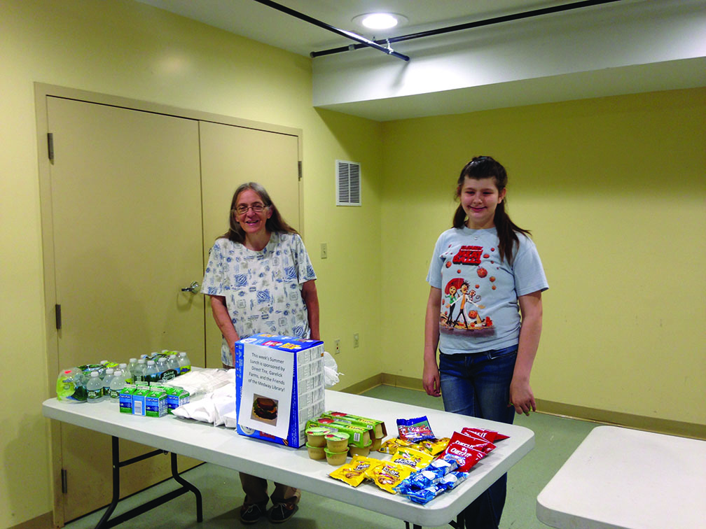 Medway Library’s pilot free lunch program, an idea conceived by library director Margaret Perkins, left, who is shown here helped out by 12-year-old Bella, is supported by the Friends of the Medway Library, and a number of local businesses, organizations and individuals. A few spots are still available.