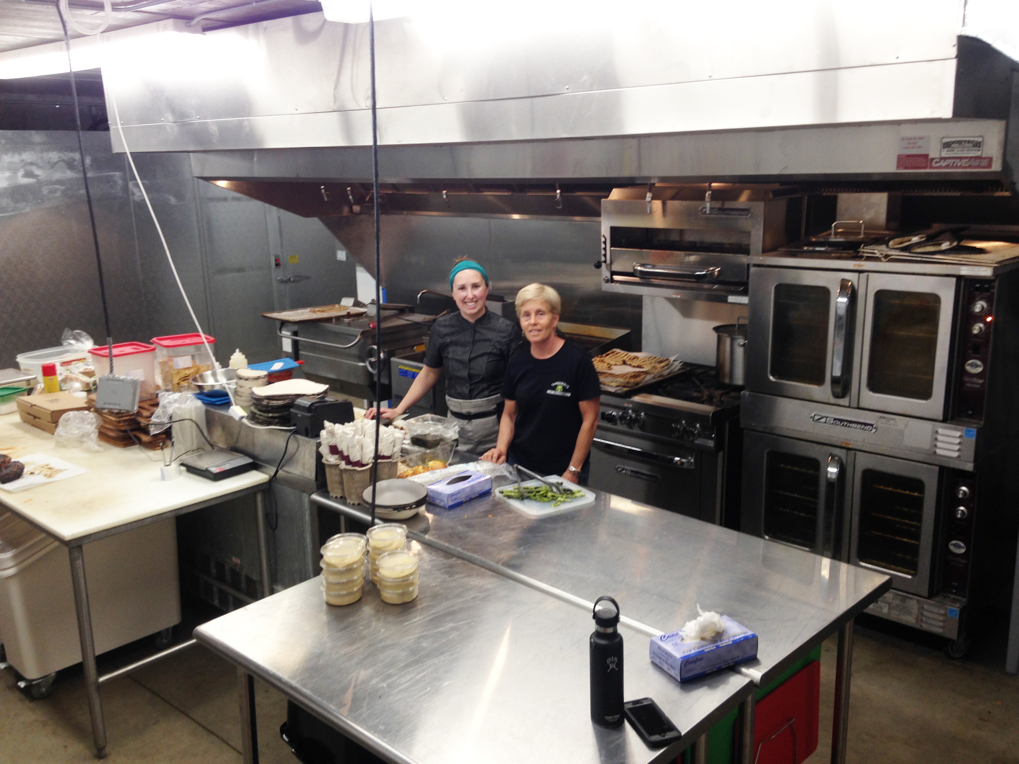 Shown is Laura Tangerini, right, with her head chef, in the newly-built kitchen underneath The Farmer’s Porch at Tangerini’s Farm, which will offer a lunch menu of locally produced food.  Tangerini’s will host a school year-end summer-start bash on June 19th, with a concert by the Phat Daddies at 6 p.m.